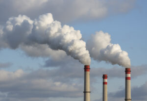 Industrial smokestacks emitting dense white smoke into a blue sky, illustrating air pollution from thermal oxidation systems