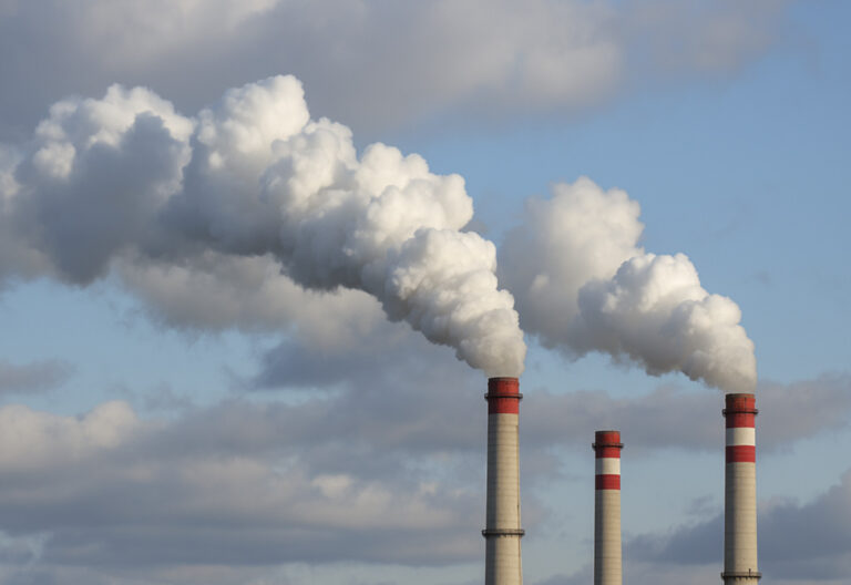 Industrial smokestacks emitting dense white smoke into a blue sky, illustrating air pollution from thermal oxidation systems